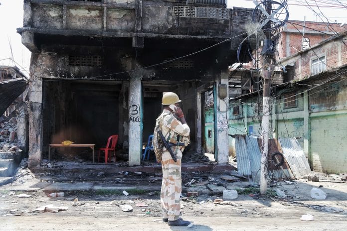 चूड़ाचांदपुर के पहाड़ी जिले में कई जली हुई और खोखली संपत्तियों में से एक के बाहर खड़ा सीआईएसएफ का एक अधिकारी | सूरज सिंह बिष्ट/दिप्रिंट