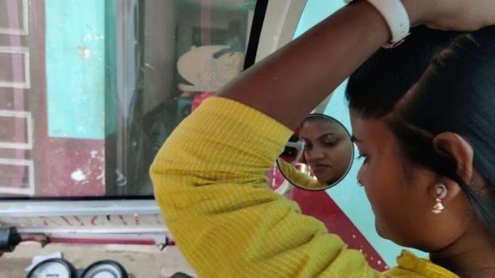 आरती अपने पिंक ई-रिक्शा के साइड व्यू मिरर में देखकर अपने बाल संवारते हुए | फोटो: दानिशमंद खान/दिप्रिंट