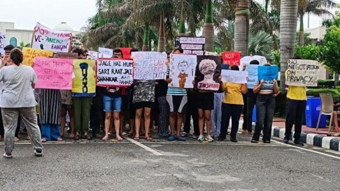 कुलपति के इस्तीफे की मांग करते हुए पोस्टर पकड़े RGNUL के मुख्य गेट के सामने खड़े छात्र | फोटो: अलमिना खातून/दिप्रिंट